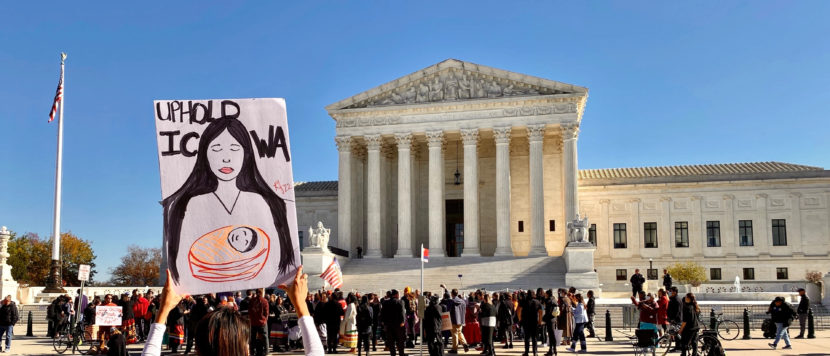 A group gathered in front of the U.S. Supreme Court building. A pair of hands is holding up a sign that says "Uphold ICWA"