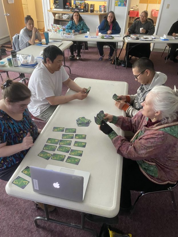 Adults and children sit around tables looking at numeral system cards