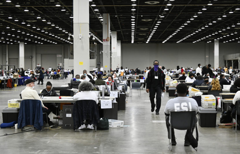 Election workers around tables in a large vote-counting facility