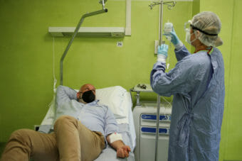 A man lies on a hospital bed watching a health worker prepare an IV bag