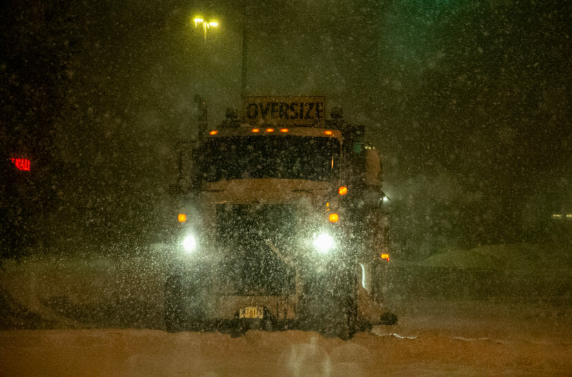 A truck driving in the dark. largely obscured by heavy falling snow.