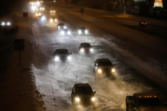 A double row of cars driving in the dark as heavy snow falls.