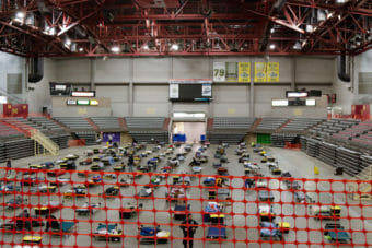 Cots arranged in rows on the floor of an arena.