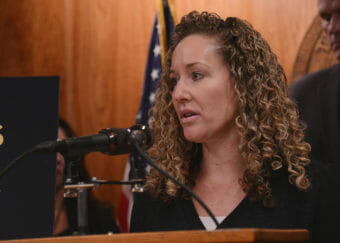 A closeup of a woman standing at a lectern and speaking into a microphone