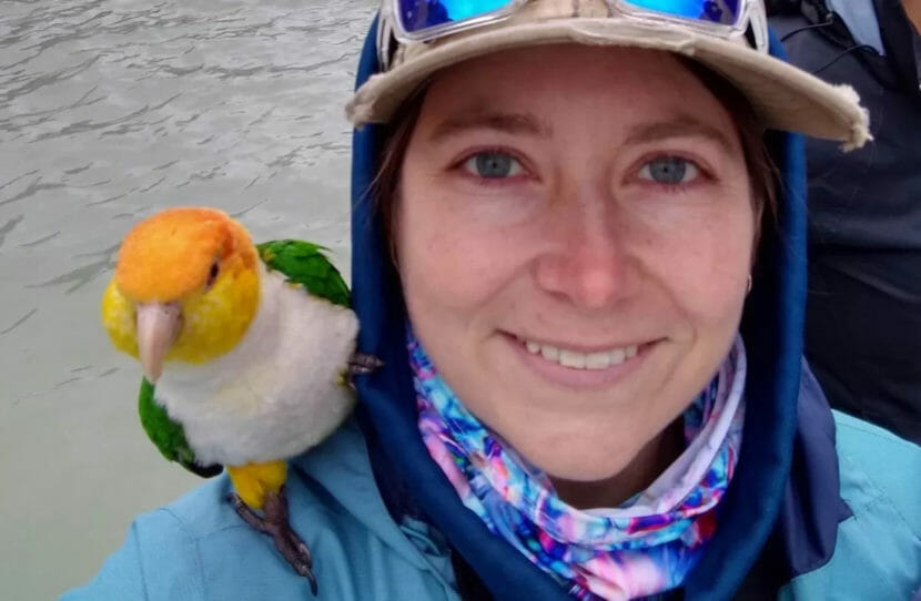 A young woman in rain gear with a parrot on her shoulder.