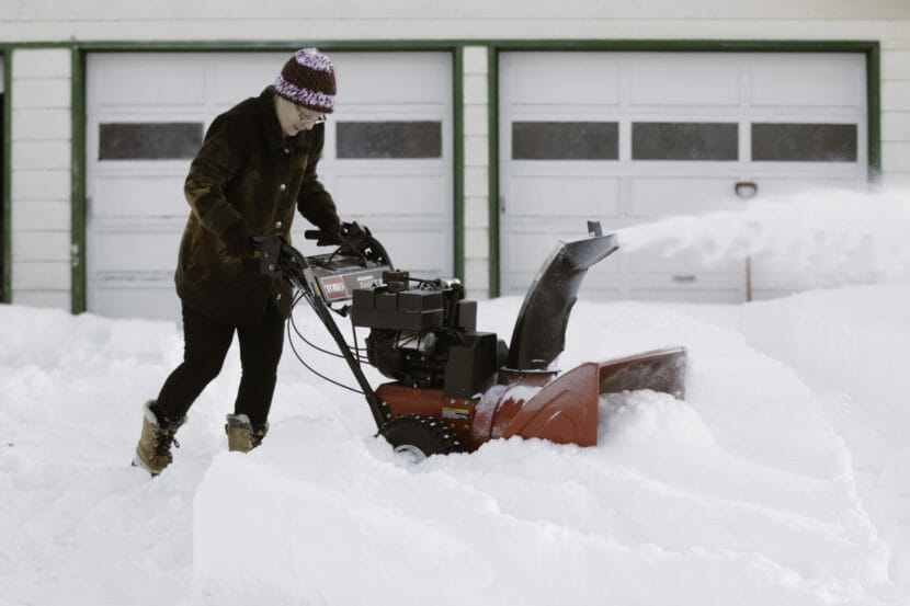 A bundled-up woman using a snowblower in very deep snow.