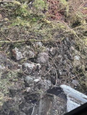 A close-up photo of the tread from a piece of heavy machinery next to an old, overgrown rock wall.