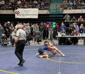 A ref stands watching two girls wrestle.