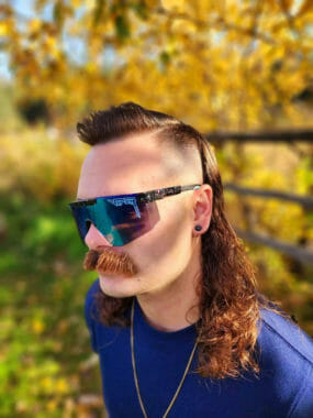 A man wearing mirror shades, and bushy mustache, and an extremely long mullet