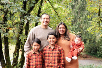 A family photo of a couple and three children standing among trees.