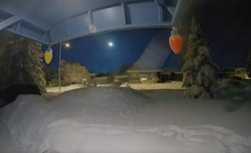 A bright white light in the sky, seen from a doorbell camera on a house along a snowy street.