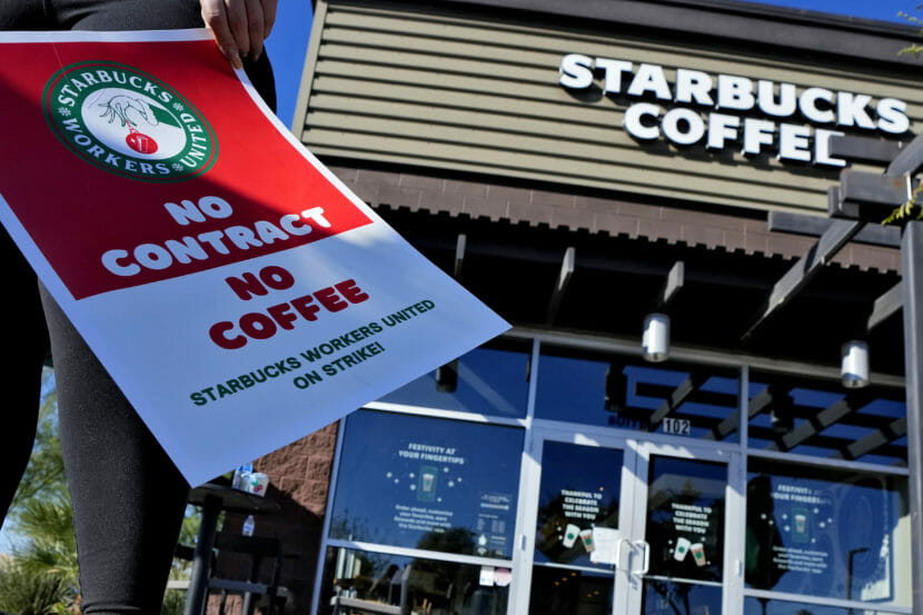 A person stands in front of a Starbucks holding a sign that says "no contract, no coffee"