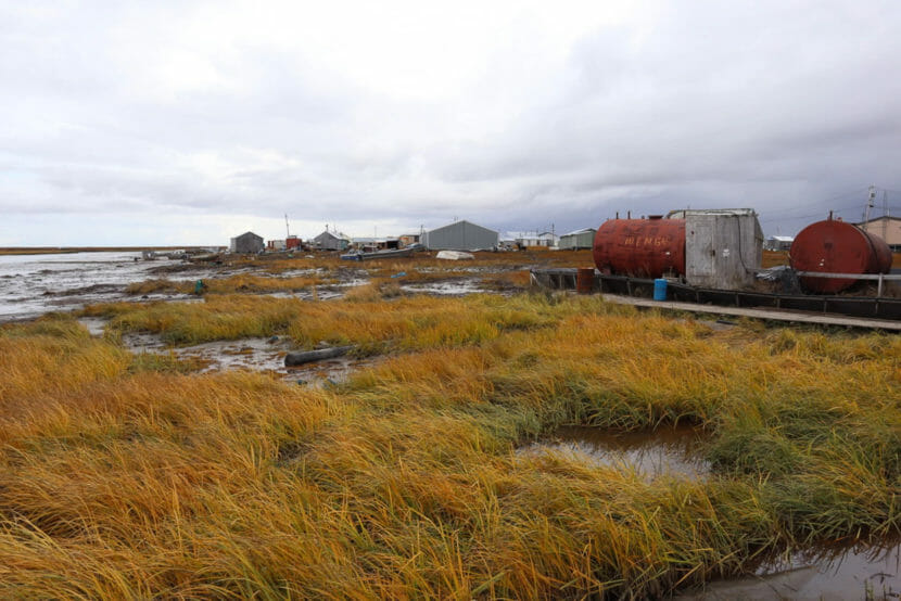 Fuel tanks stand amid flooded shoreline on the edge of a village.