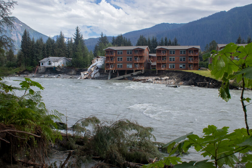 The remnants of a destroyed house sits between another house and condo buildings in the 4400 block of Riverside Drive left hanging precariously over the Mendenhall River after their foundations were eroded away during record high water from a glacial outburst flood on Saturday August 5th, 2023. (Mikko Wilson / KTOO)