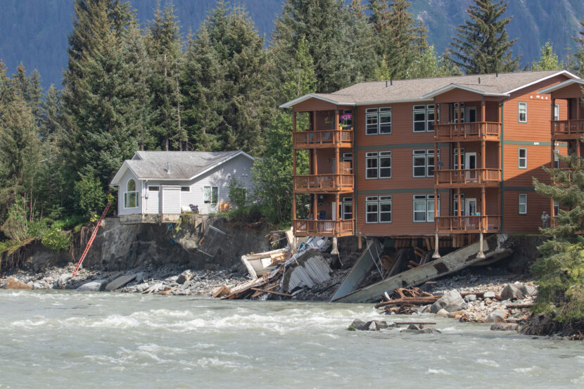 A house and condo buildings in the 4400 block of Riverside Drive hang precariously over the Mendenhall River after their foundations were eroded away during record high water from a glacial outburst flood on Saturday August 5th, 2023. (Mikko Wilson / KTOO)