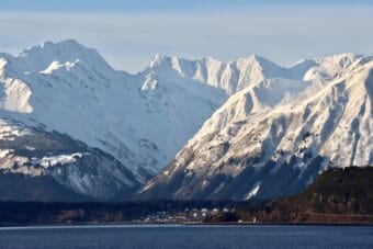 A wall of steep, snow-covered mountains rises behind a small, Alaska town