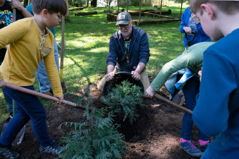 Ben Patterson loosens a yellow cedar sapling from its pot as children shovel soil at Evergreen Cemetery on Arbor Day. (Alix Soliman/KTOO)