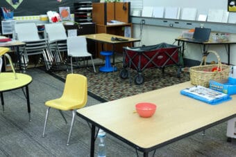 A wooden table with a red plastic bowl and blue clipboard next to a small yellow chair.