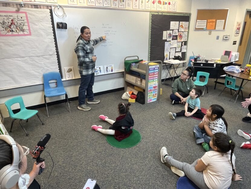X̱'unei Lance Twitchell points at writing on a whiteboard in front of Pre-kindergarten students.
