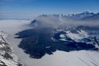 An aerial photo of a massive landslide that's come down onto a glacier from snowy mountains.