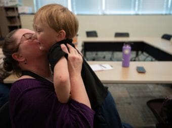 A mom embraces her child with a hug and a kiss.