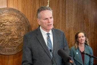 Man speaking into microphones in wood-paneled room