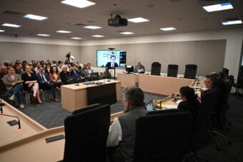 A hearing room. Public section is full.