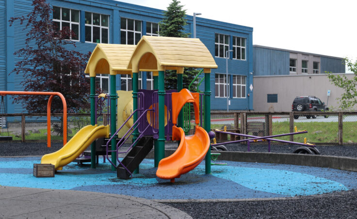 A green metal play structure with two slides on a blue rubber flooring.