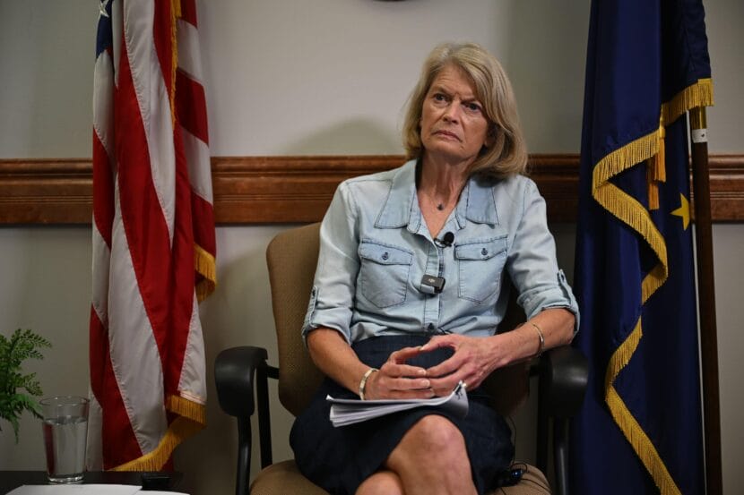 a woman in a chair with the u.s. and alaska flag behind her
