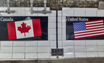 A vertical black line on the inner wall of the Detroit-Windsor Tunnel marks the border between Canada and the United States. On the left side of the line is a Canadian flag, and on the right side of the line is an American flag.