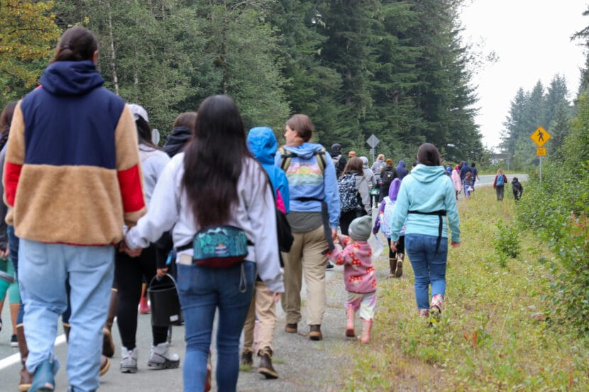A couple holds hands in the back of a large group of people walking near a road.
