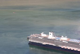 Smoke can be seen rising from the stack of a large cruise ship