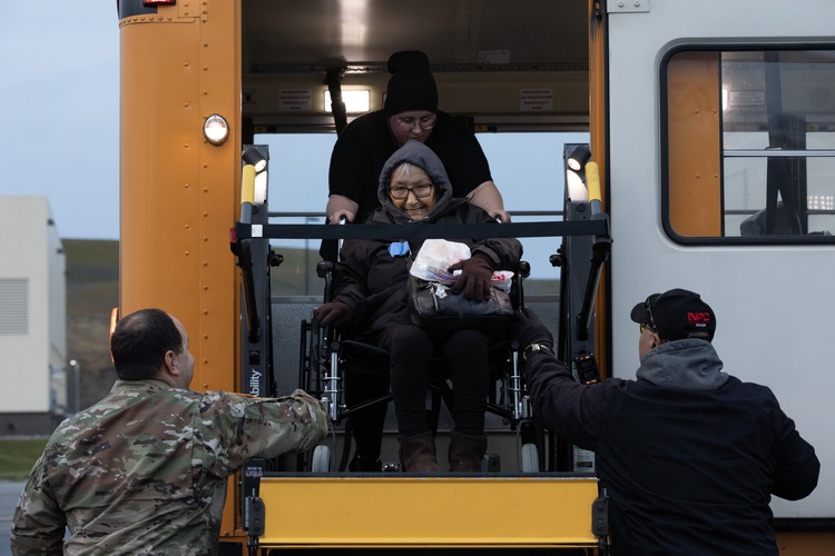 People in uniform help a woman in a wheelchair down from a bus ramp