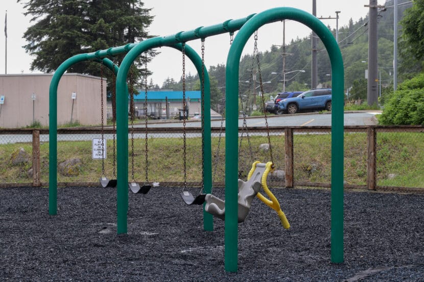 A green metal swingset with three regular black swings and a plastic child's seat.