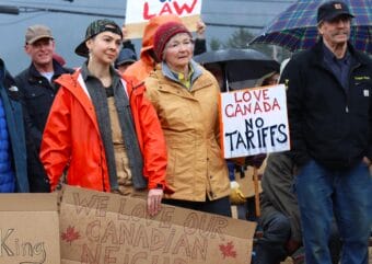 A group of people standing outdoors holding signs supporting Canada and disapproving of tariffs.