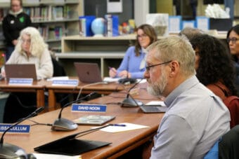 Steve Whitney sits in front of a partially closed laptop on a wooden table with his face half in view.