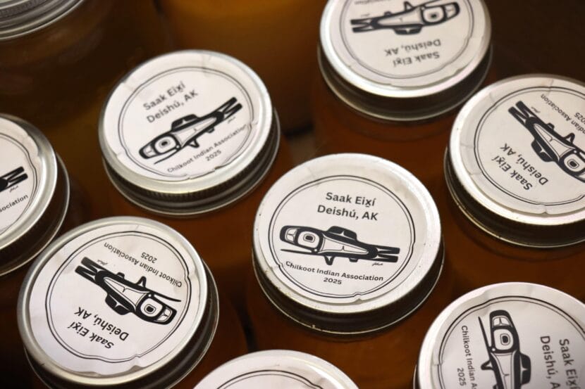 The tops of several canning jars, labeled with stickers showing a formline illustration of a fish and the words "Saak Eix̲í"