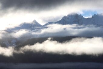 An eagle soars in the skies in front of a cloudy mountain range.