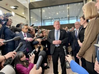 A group of dignitaries face a gaggle of reporters