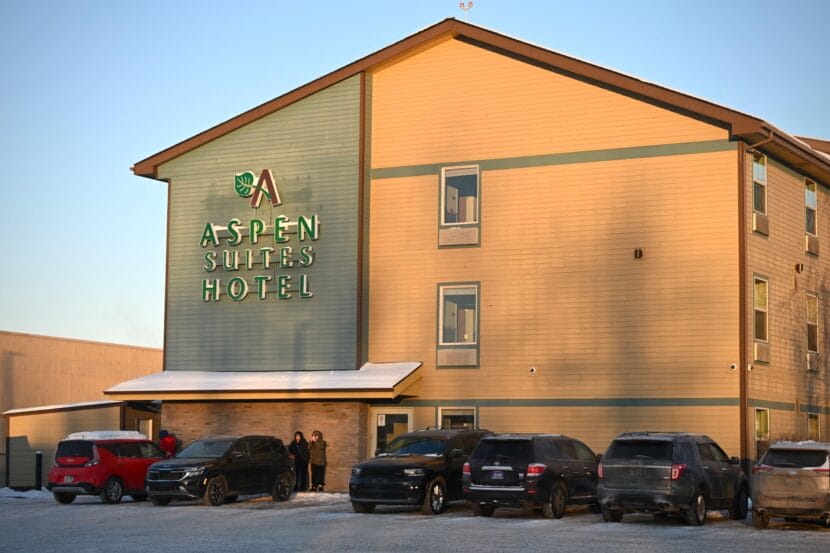 People stand outside a hotel with cars are parked in front