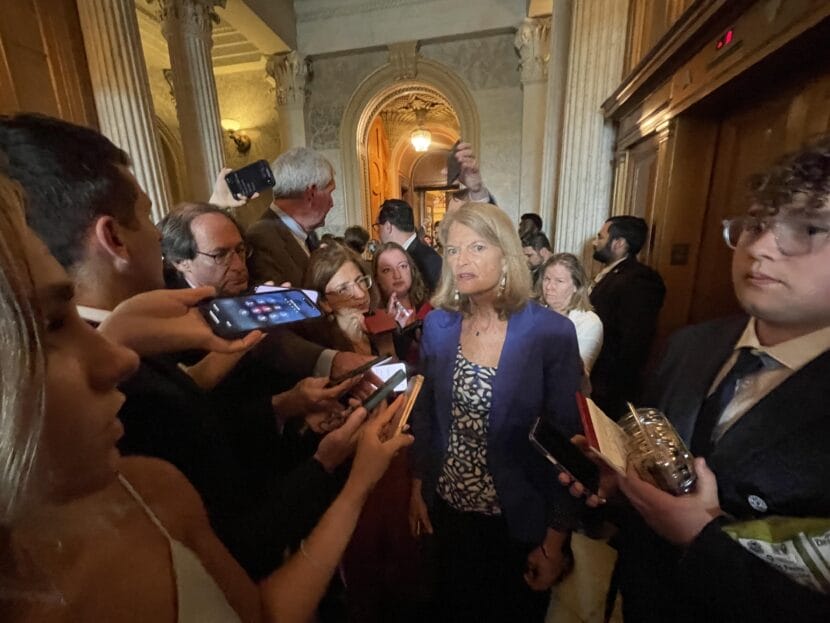 woman surrounded by people extending their iphones to her, aimed at her face