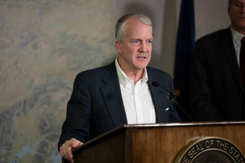 A man in a black suit stands at a podium talking into a microphone.