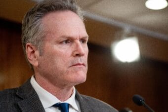 Man in grey suit standing behind microphones
