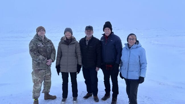 Five people in a snowy landscape, one in a military uniform