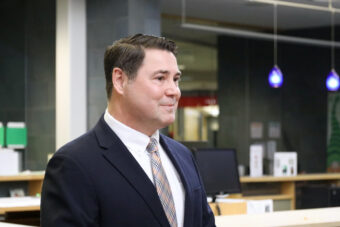 Shawn Arnold stands in a library looking to the right, dressed in a black suit.