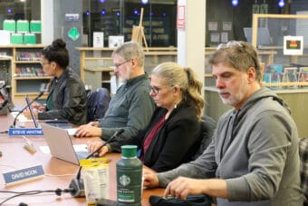 For school board members sit at a wooden table with computers, snacks and beverages.