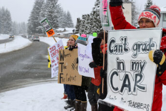 People stand on a snow-filled sidewalk holding signs saying "Can't grade in my car," "Negotiate now" and "Where's the fair contract."