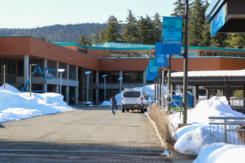 A person walks on a paved path with piles of snow on either side.