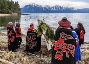 Tribal citizens wearing regalia (the Séet Ká Kwáan dance group) drum and sing around Petersburg’s new canoe.