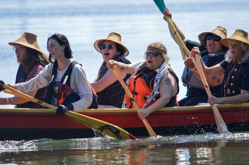 Paddlers in cedar woven hats sing as they paddle aboard the Wind Dancer, a traditional canoe built using new methods for carvers, sailing to Auke Recreation Area. June 2, 2026.
